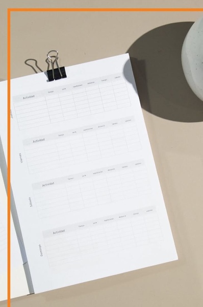 A high-quality top-down shot of a printed fitness planning sheet held by a binder clip, showcasing a clean, organized, and professional aesthetic.